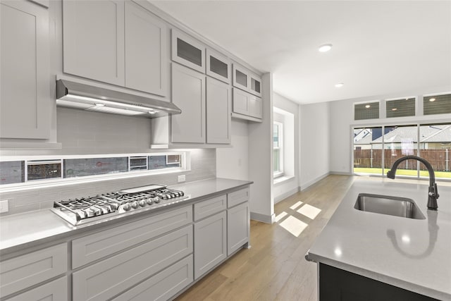 kitchen featuring stainless steel gas stovetop, sink, tasteful backsplash, gray cabinets, and light wood-type flooring