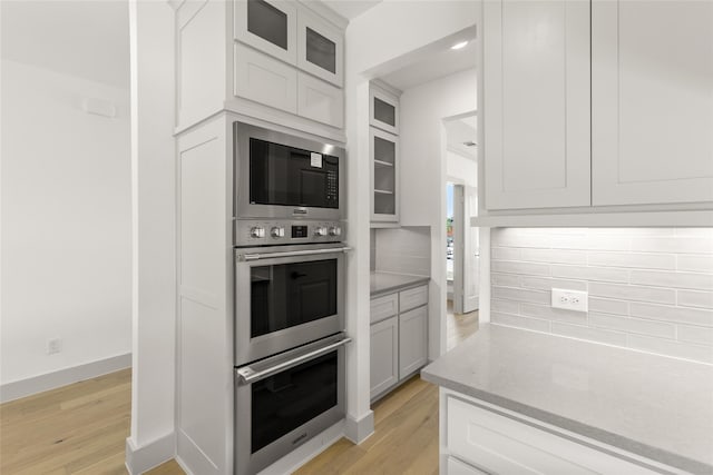 kitchen with white cabinetry, light hardwood / wood-style flooring, tasteful backsplash, and stainless steel double oven