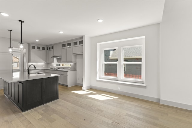 kitchen with light hardwood / wood-style floors, a center island with sink, sink, gray cabinets, and decorative light fixtures