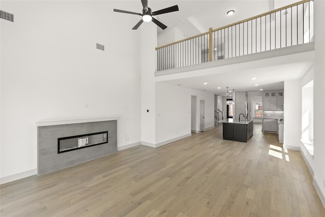 unfurnished living room with light hardwood / wood-style floors, a towering ceiling, sink, ceiling fan, and a fireplace