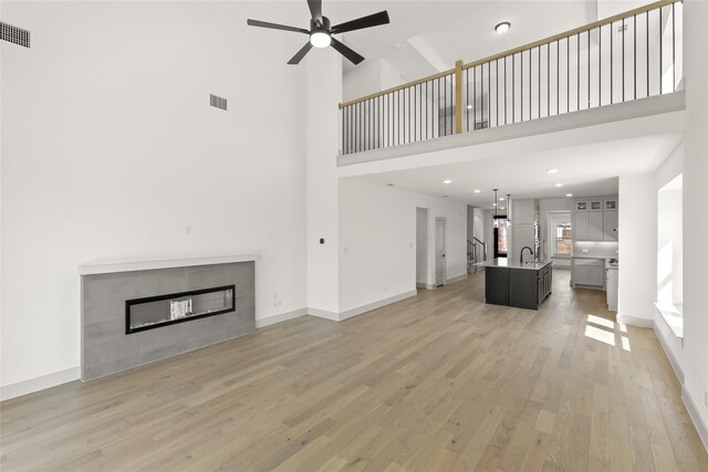 5249 Deep Creek Dr, Fort Worth, TX 76179 - unfurnished living room featuring a sink, light wood-style flooring, a tiled fireplace, ceiling fan, and a high ceiling