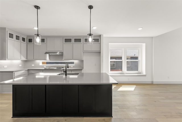 kitchen featuring tasteful backsplash, pendant lighting, sink, an island with sink, and light hardwood / wood-style floors