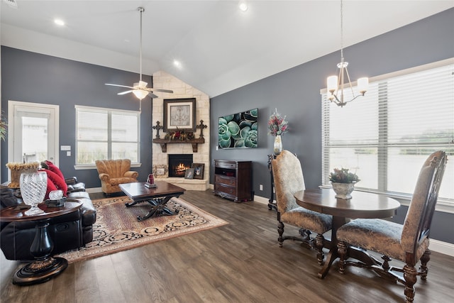 living room featuring ceiling fan with notable chandelier, dark hardwood / wood-style floors, a stone fireplace, and lofted ceiling