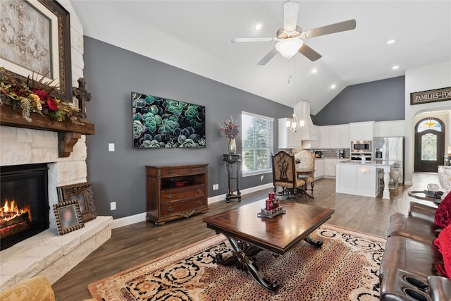 living room with a stone fireplace, high vaulted ceiling, dark wood-type flooring, and ceiling fan with notable chandelier