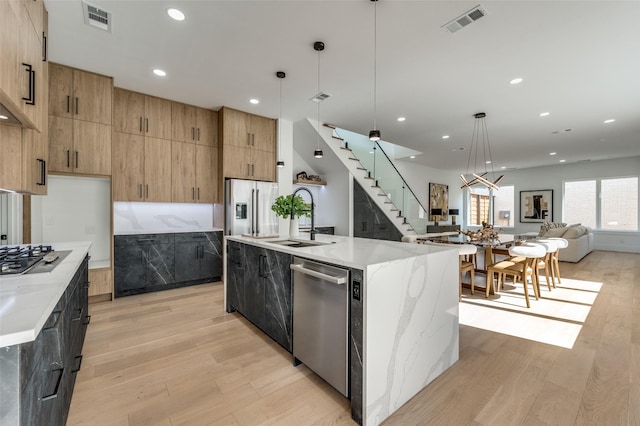 kitchen featuring light stone countertops, a large island, light hardwood / wood-style floors, pendant lighting, and appliances with stainless steel finishes