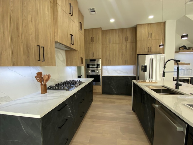 kitchen featuring pendant lighting, sink, light hardwood / wood-style floors, light stone counters, and stainless steel appliances