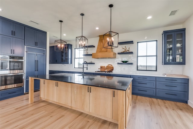 kitchen featuring stainless steel appliances, a kitchen island with sink, sink, blue cabinetry, and an inviting chandelier