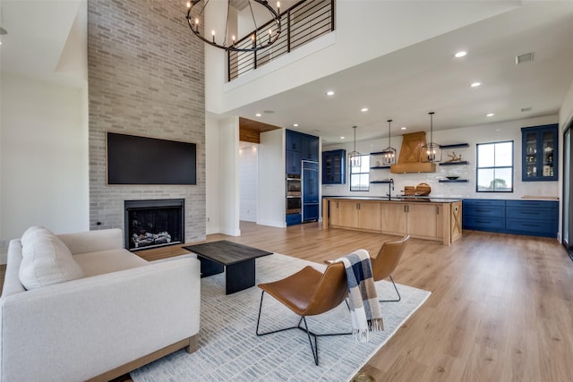 living room featuring a chandelier, light hardwood / wood-style floors, sink, and a brick fireplace