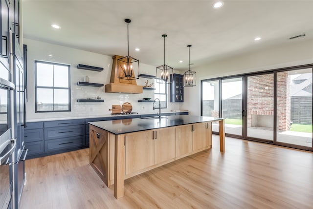 kitchen with sink, an island with sink, hanging light fixtures, and light hardwood / wood-style floors