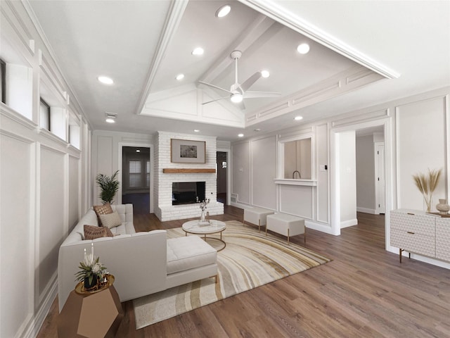 living room featuring a raised ceiling, crown molding, a brick fireplace, ceiling fan, and wood-type flooring