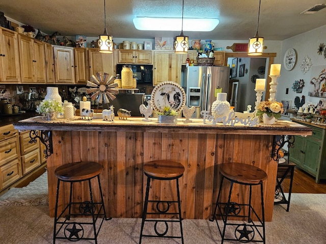 kitchen featuring pendant lighting, a center island, stainless steel refrigerator with ice dispenser, a textured ceiling, and a kitchen bar