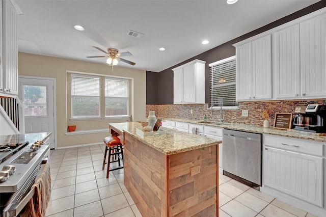 kitchen with light stone counters, stainless steel appliances, sink, white cabinets, and a center island