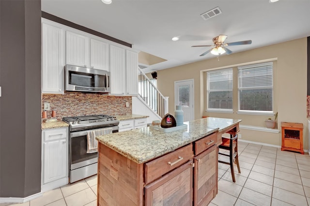 kitchen featuring a center island, backsplash, light tile patterned floors, white cabinetry, and stainless steel appliances