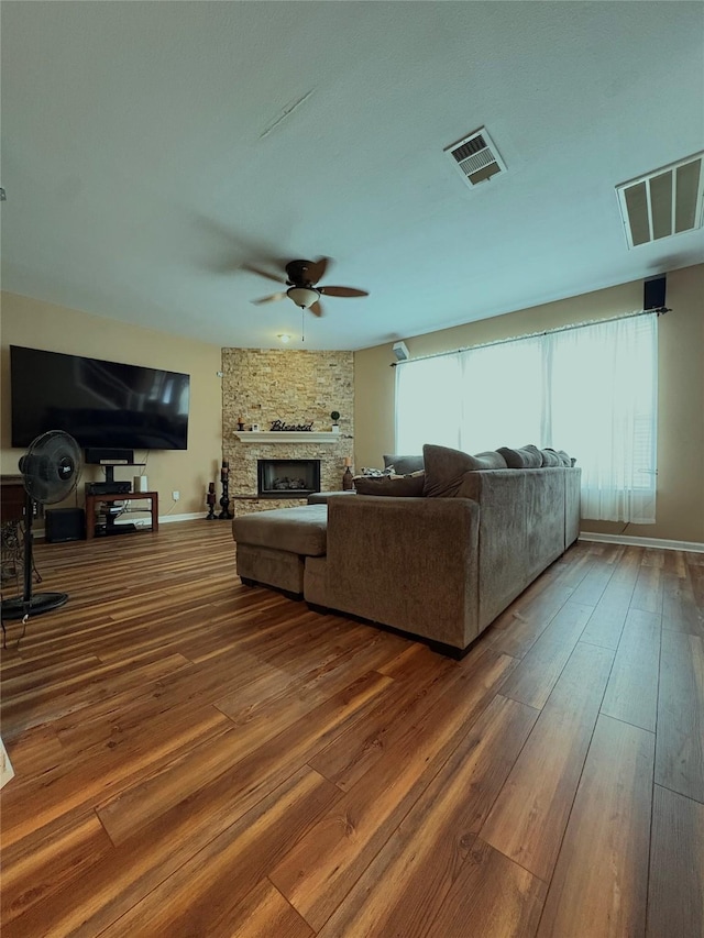 living room featuring wood-type flooring, a stone fireplace, visible vents, and a ceiling fan