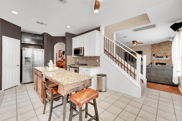 kitchen with ceiling fan, a fireplace, light tile patterned flooring, and appliances with stainless steel finishes