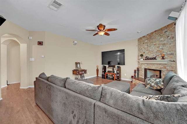 living room featuring ceiling fan, a stone fireplace, and light wood-type flooring