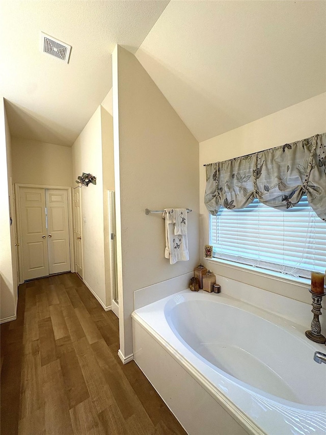 full bathroom featuring vaulted ceiling, wood finished floors, visible vents, and a garden tub