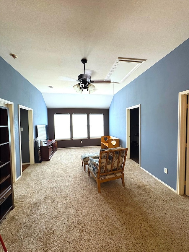 living area with attic access, a ceiling fan, a textured ceiling, and light colored carpet