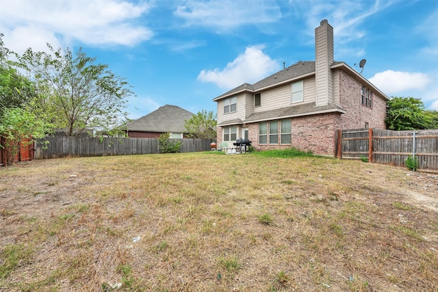 back of property featuring brick siding, a yard, a chimney, and a fenced backyard