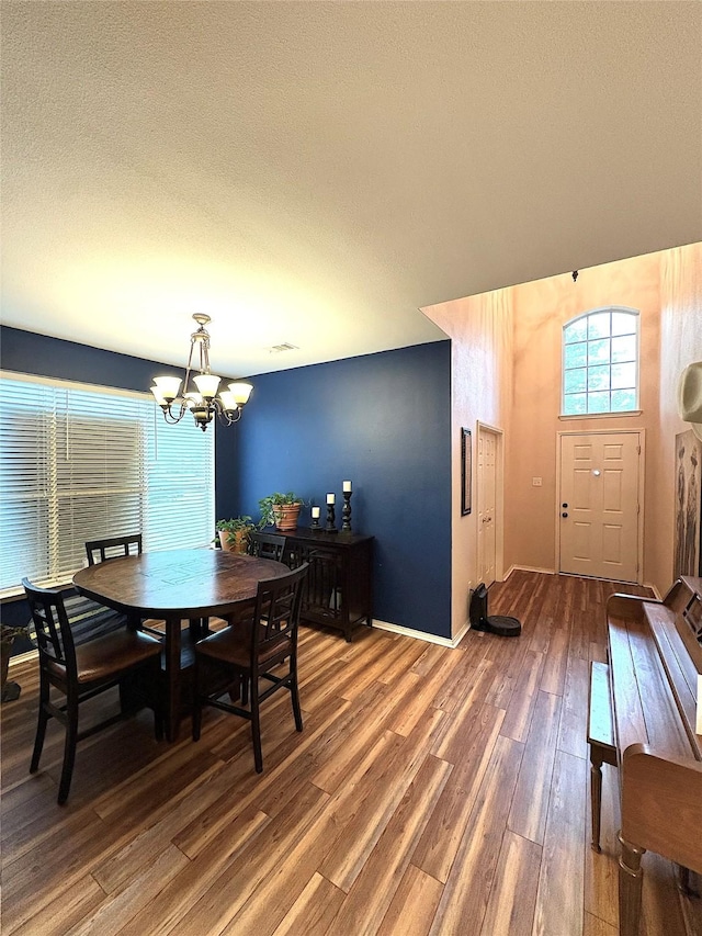 dining space with wood finished floors, a textured ceiling, baseboards, and a notable chandelier
