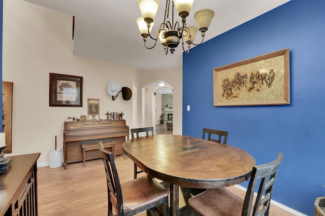 dining room with arched walkways, a notable chandelier, light wood finished floors, and baseboards