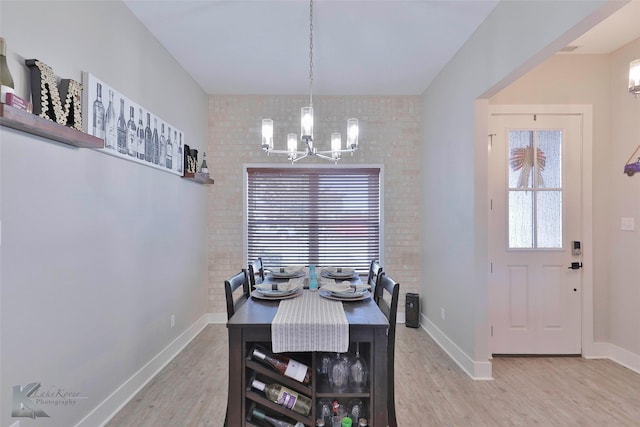 dining area featuring light wood-type flooring, a notable chandelier, and brick wall