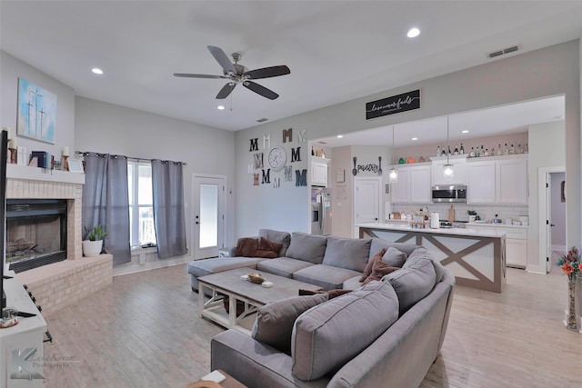 living room featuring ceiling fan, light hardwood / wood-style flooring, and a brick fireplace