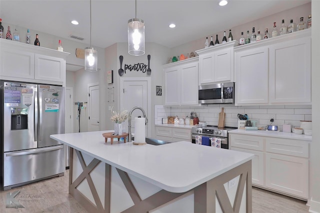 kitchen with a kitchen island with sink, white cabinets, sink, tasteful backsplash, and stainless steel appliances