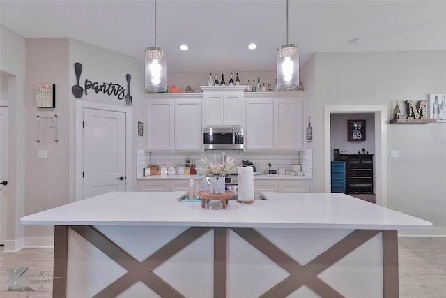 kitchen with a center island with sink, white cabinetry, and hanging light fixtures