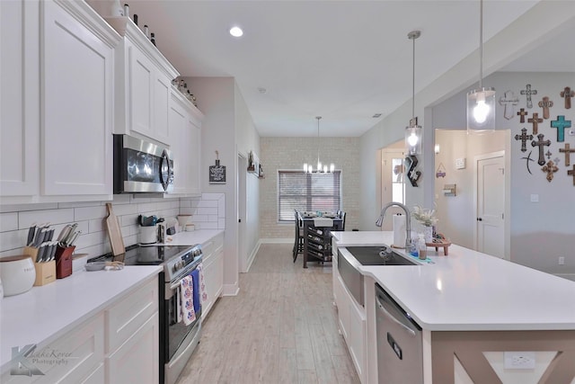 kitchen featuring white cabinets, decorative light fixtures, stainless steel appliances, and a kitchen island with sink