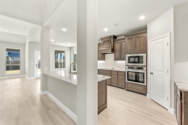 kitchen with light stone counters, custom exhaust hood, black appliances, and light wood-type flooring