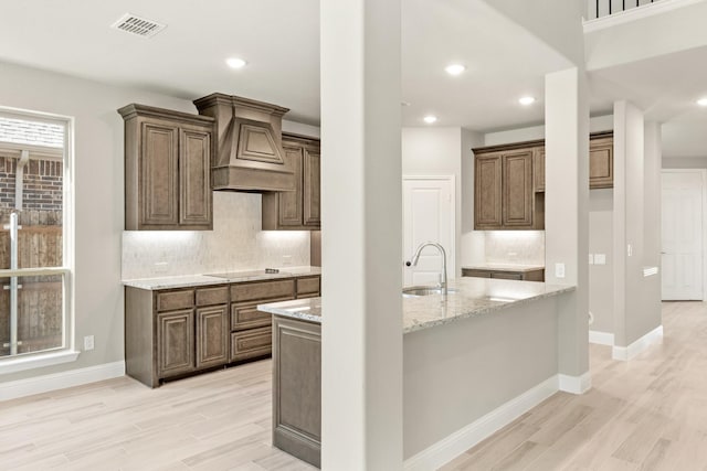 kitchen featuring sink, tasteful backsplash, black electric stovetop, custom range hood, and light wood-type flooring