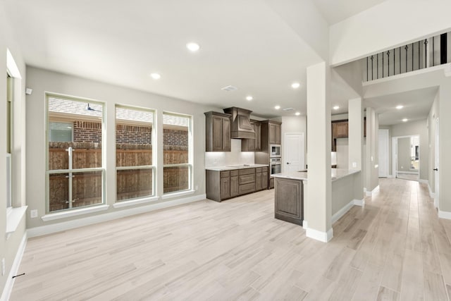 kitchen with stainless steel microwave, premium range hood, light hardwood / wood-style flooring, stovetop, and kitchen peninsula