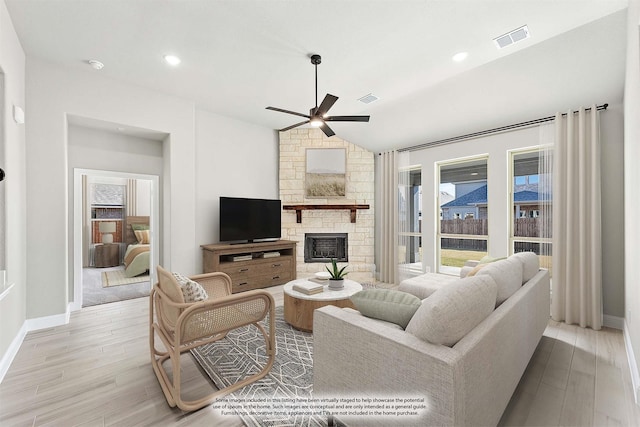 living room featuring ceiling fan, a stone fireplace, vaulted ceiling, and light wood-type flooring