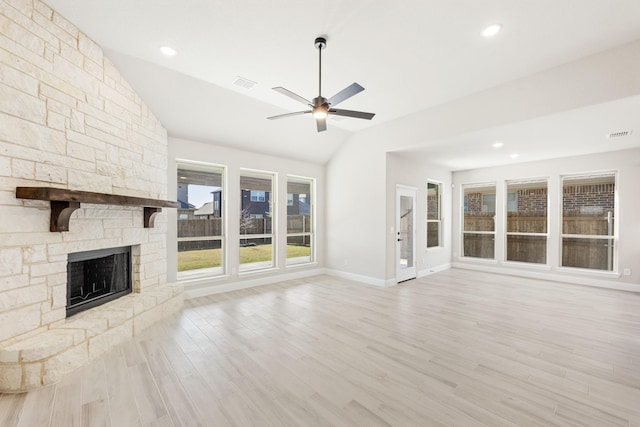 unfurnished living room with ceiling fan, a stone fireplace, lofted ceiling, and light hardwood / wood-style flooring