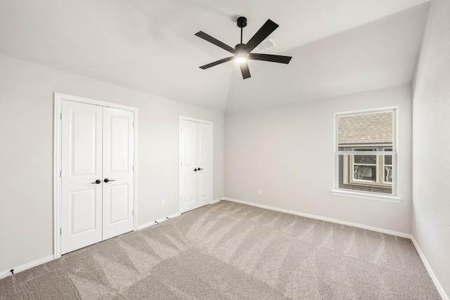 unfurnished bedroom with carpet, ceiling fan, lofted ceiling, and multiple closets