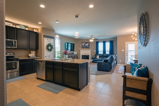 kitchen with hanging light fixtures, ceiling fan with notable chandelier, sink, appliances with stainless steel finishes, and a kitchen island with sink