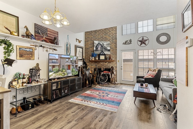 living room featuring vaulted ceiling, hardwood / wood-style floors, a fireplace, brick wall, and a notable chandelier