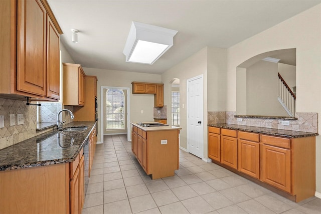 kitchen featuring sink, appliances with stainless steel finishes, dark stone countertops, a center island, and light tile patterned flooring