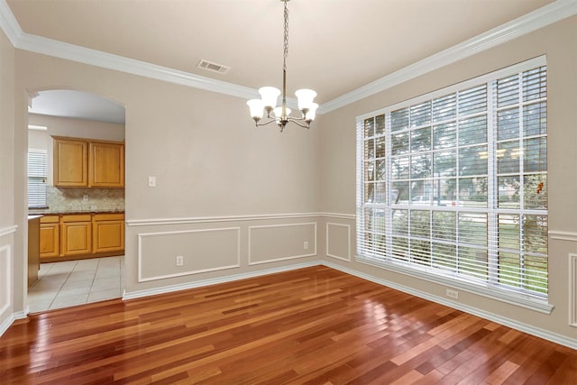 unfurnished dining area featuring ornamental molding, an inviting chandelier, and light hardwood / wood-style flooring