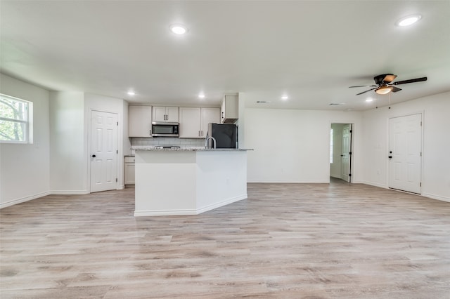 kitchen with light stone counters, light wood-type flooring, black refrigerator, decorative backsplash, and ceiling fan