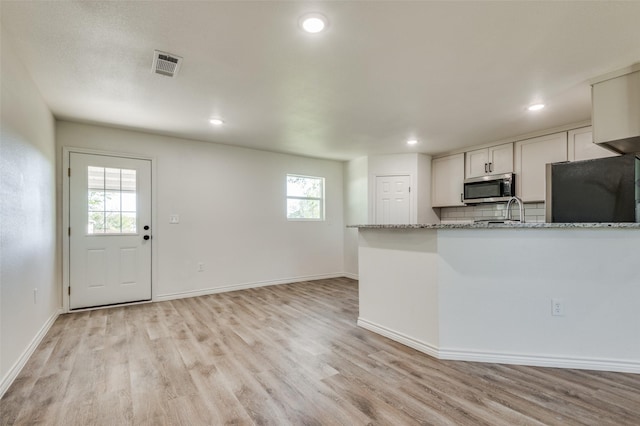 kitchen with light hardwood / wood-style floors, black fridge, sink, light stone counters, and white cabinets