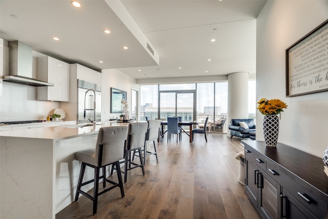 kitchen with stainless steel built in fridge, white cabinetry, a kitchen bar, wall chimney exhaust hood, and hardwood / wood-style flooring