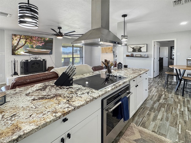 kitchen featuring stainless steel oven, pendant lighting, black electric cooktop, island range hood, and white cabinets