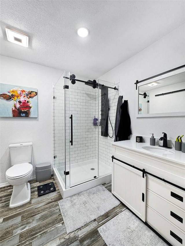 bathroom with vanity, a shower with door, hardwood / wood-style flooring, toilet, and a textured ceiling