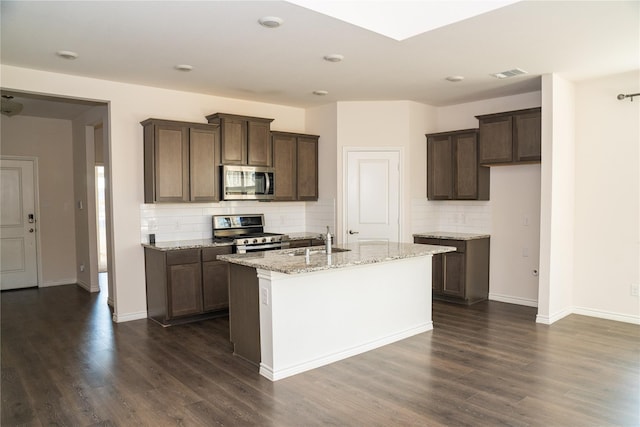 kitchen featuring stainless steel appliances, a kitchen island with sink, light stone countertops, and dark hardwood / wood-style floors