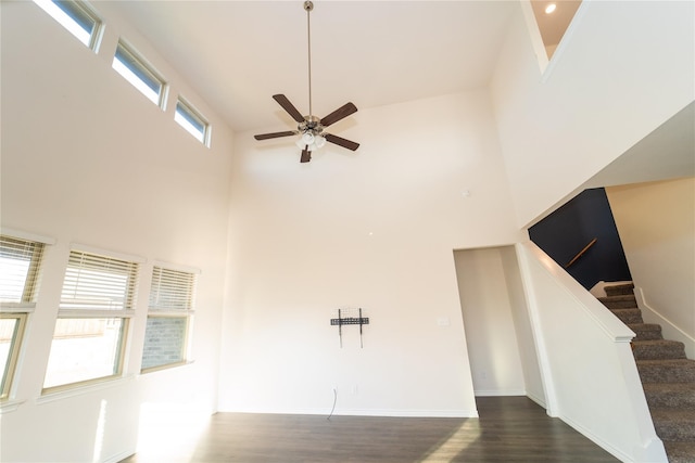 unfurnished living room featuring dark hardwood / wood-style flooring, ceiling fan, and a high ceiling