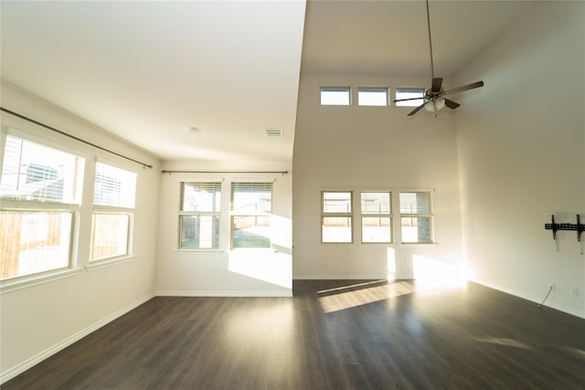 unfurnished living room featuring dark wood-type flooring, ceiling fan, and a towering ceiling