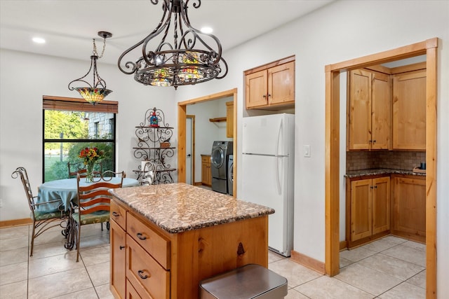 kitchen featuring light stone counters, washer / clothes dryer, pendant lighting, white fridge, and a kitchen island