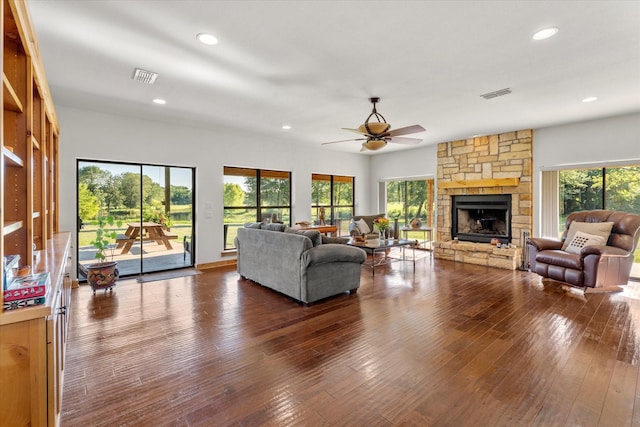 living room with dark hardwood / wood-style floors, a stone fireplace, ceiling fan, and a healthy amount of sunlight